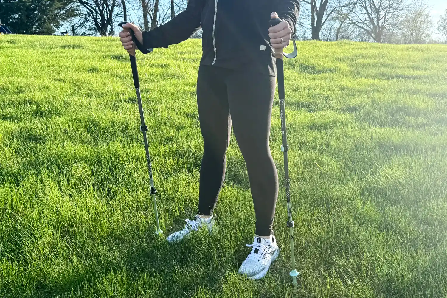A person stands in grass with the Black Diamond Pursuit Trekking Poles