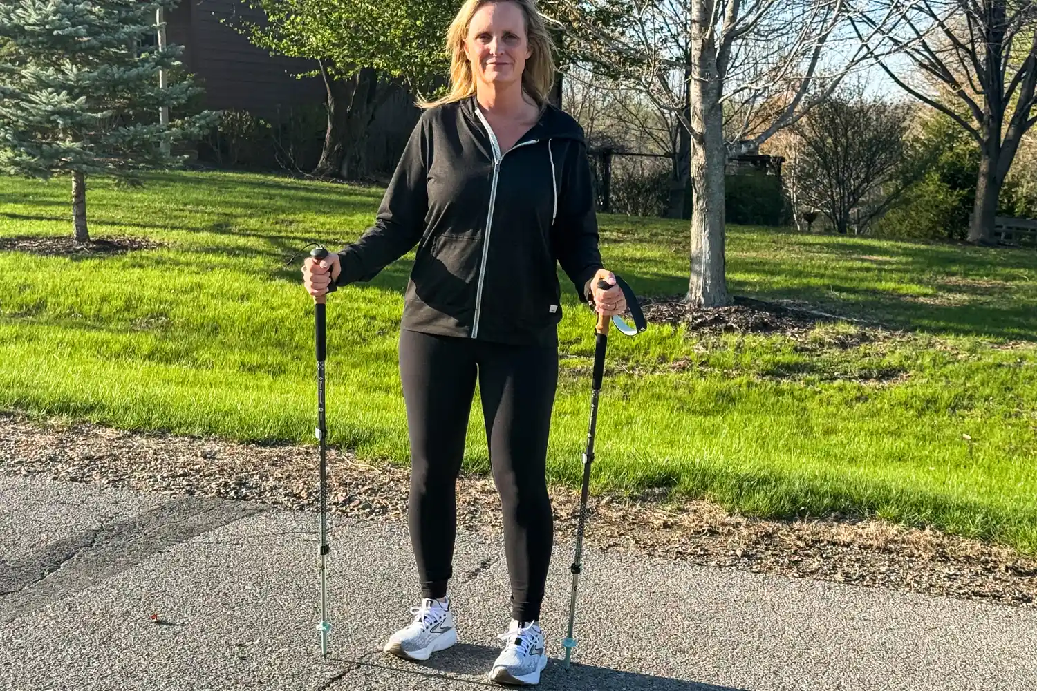 A person stands outside on asphalt while using the Black Diamond Pursuit Trekking Poles