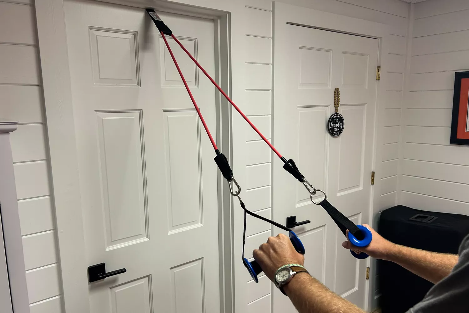 A person holding the handles of a Bodylastics Resistance Band attached to a door