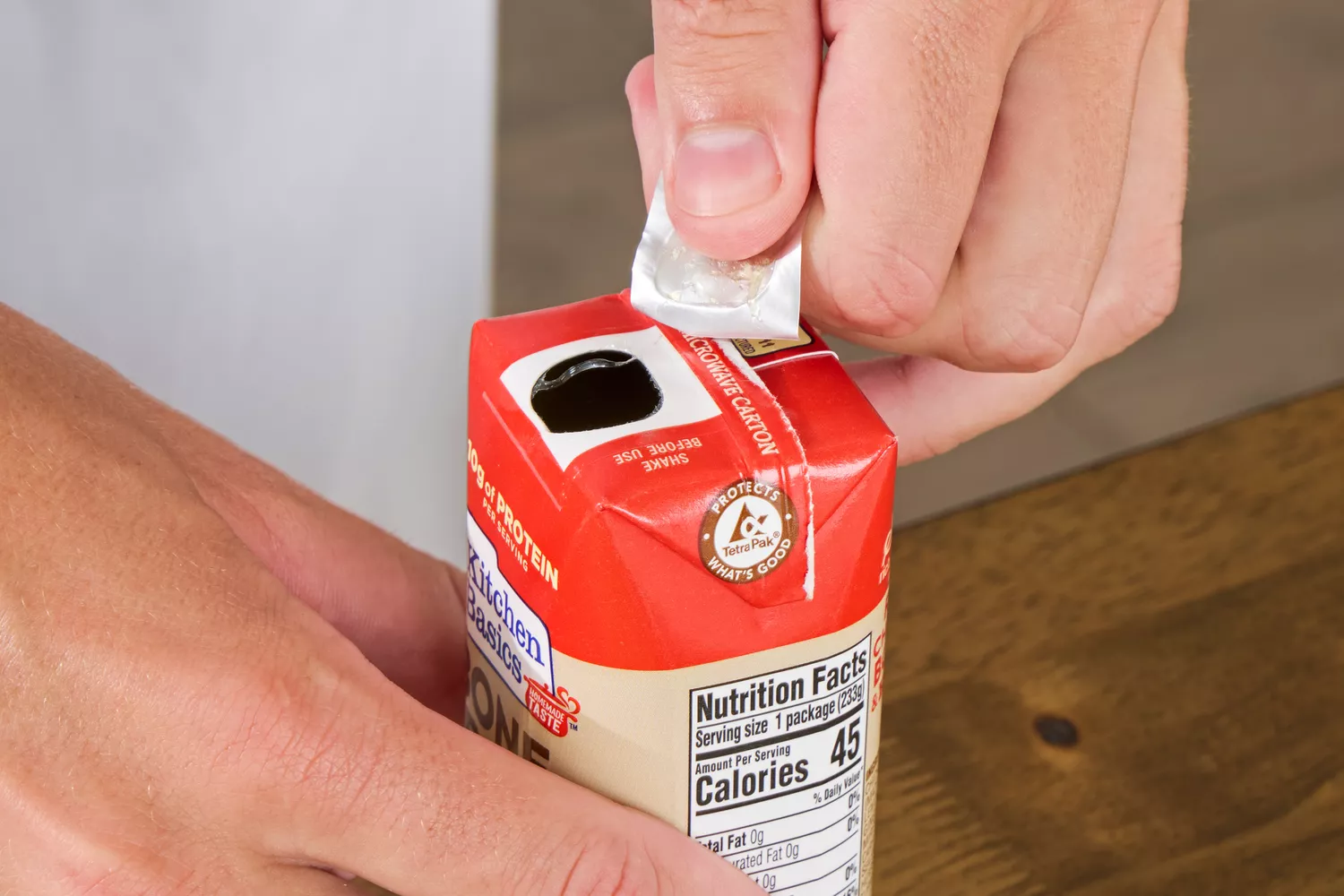A person removes the cover on the Kitchen Basics Turmeric &amp; Ginger With Lemongrass Chicken Bone Broth