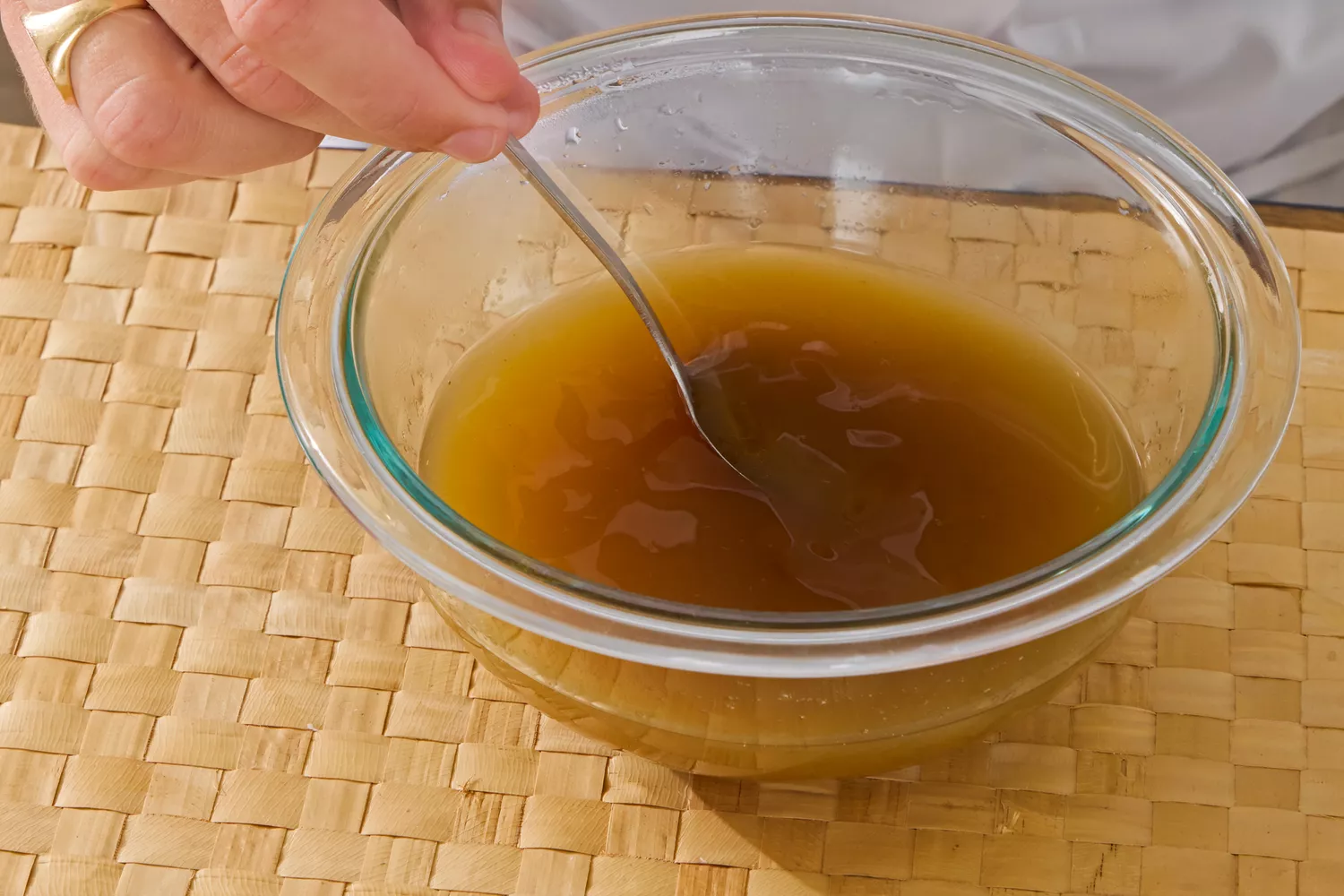A person stirs Kitchen Basics Turmeric &amp; Ginger With Lemongrass Chicken Bone Broth in a glass bowl