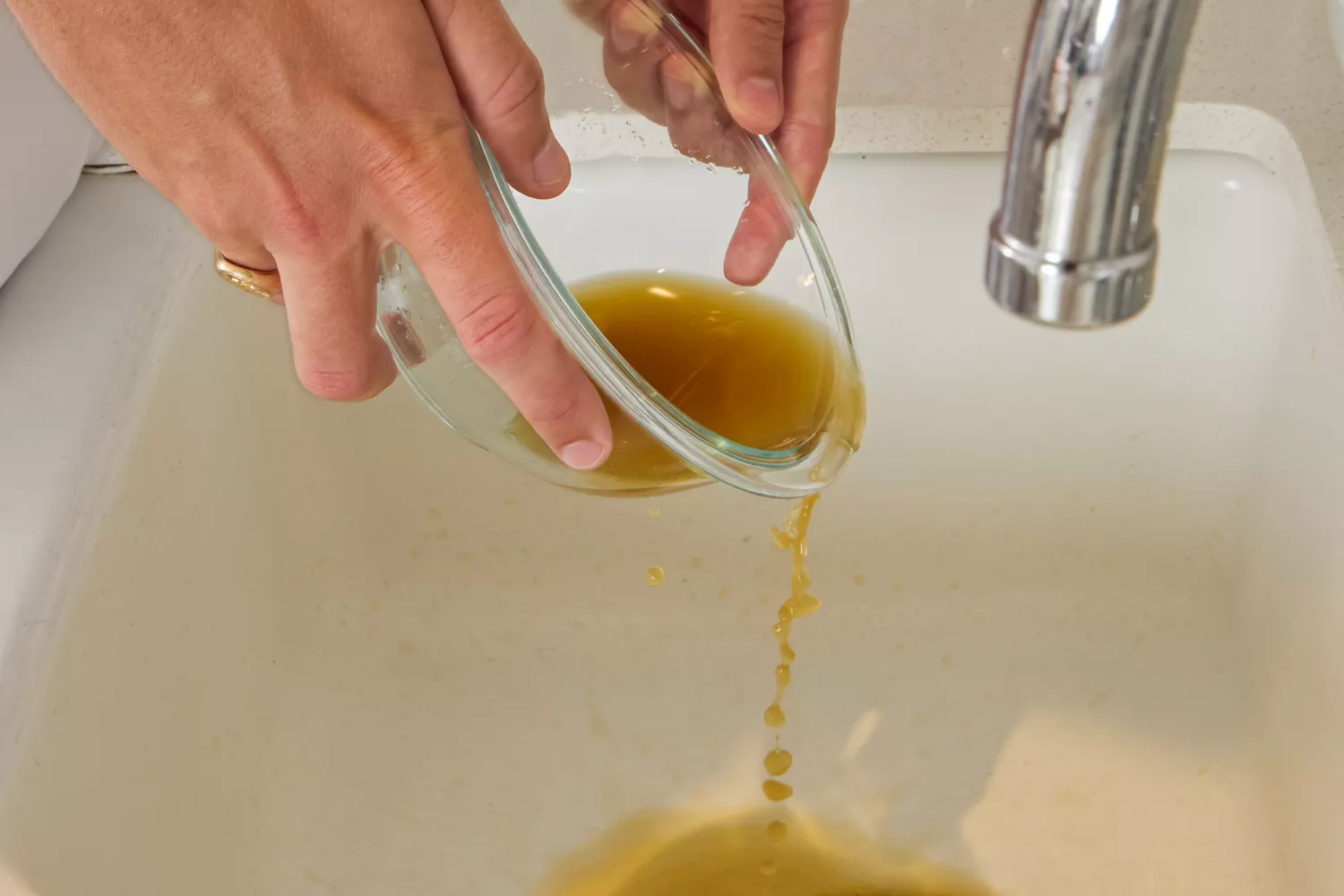 A person pours Kitchen Basics Turmeric &amp; Ginger With Lemongrass Chicken Bone Broth into a sink