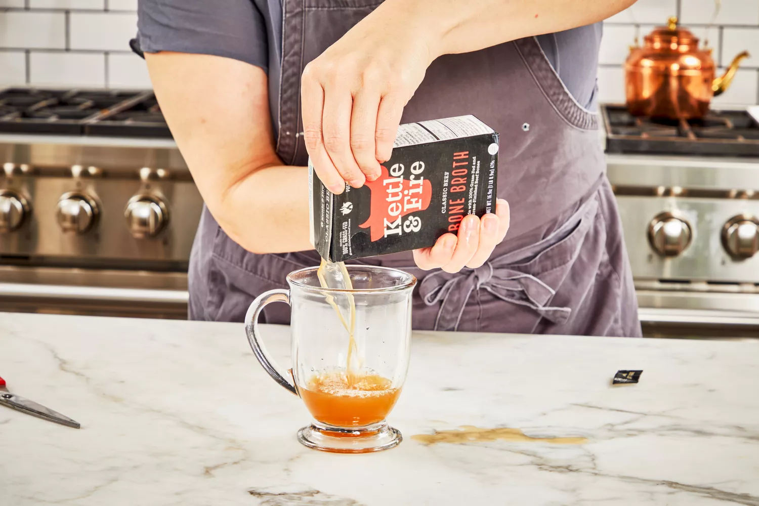 A person pours Kettle &amp; Fire Bone Broth into a glass