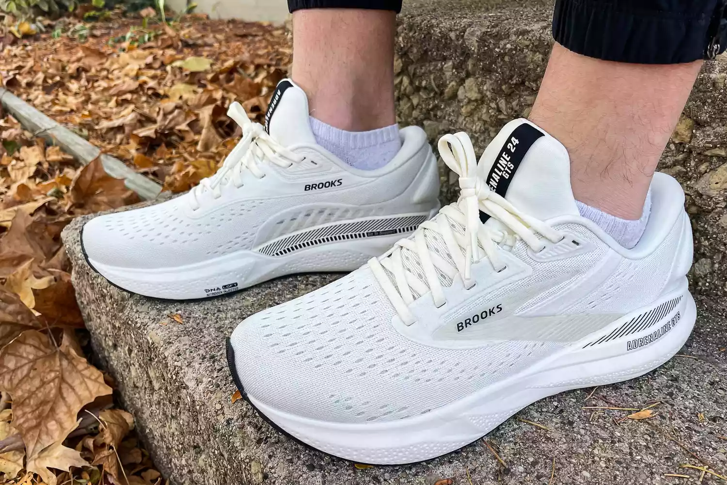 A person wears the Brooks Men's Adrenaline GTS 24 Running Shoes outside on stone