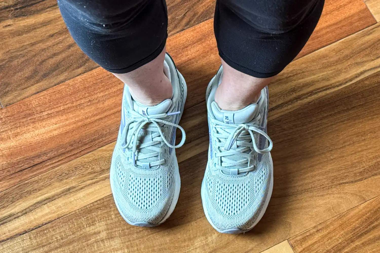 A person wears the Brooks Women's Ariel GTS 24 Running Shoes on a wooden floor