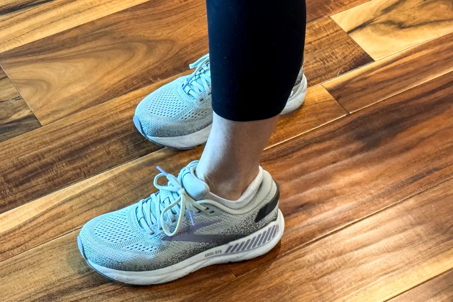 A person stands on a wooden floor while wearing the Brooks Women's Ariel GTS 24 Running Shoes