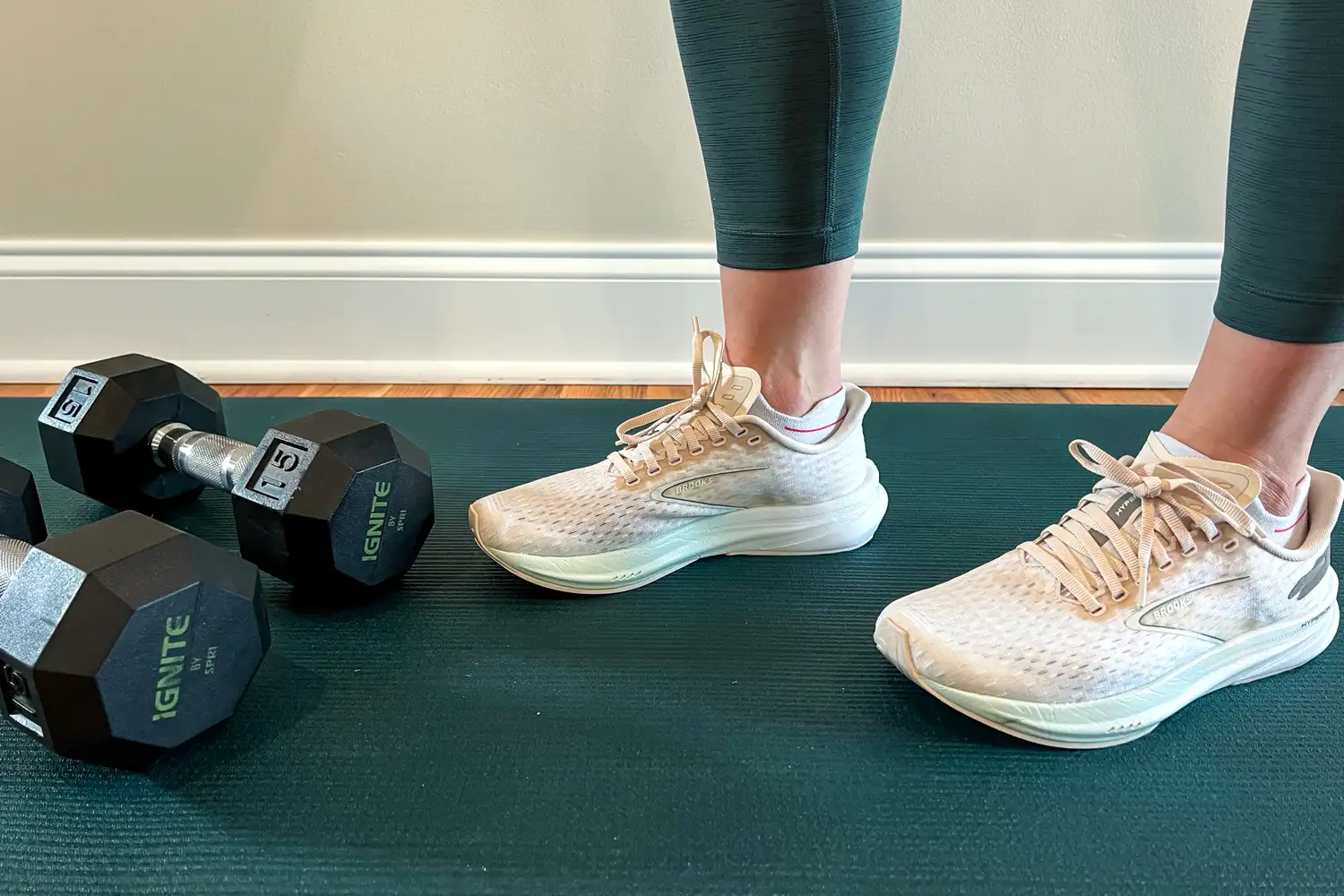 Legs in workout attire on a gym mat near 15-pound dumbbells