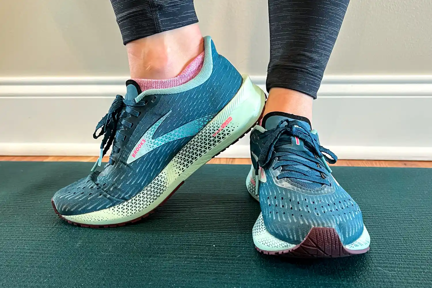 Close-up of someone's feet wearing running shoes on a yoga mat, showing the design and fit of the footwear