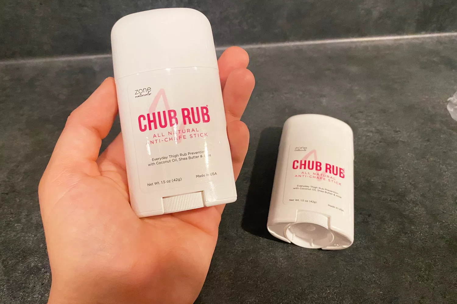 A person holds a stick of Zone Naturals Chub Rub All-Natural Anti-Chafing Stick