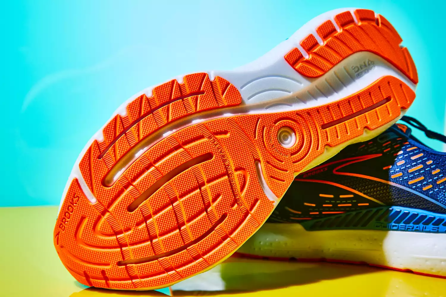 The sole of the Brooks Men's Glycerin GTS 20 Running Shoe against yellow and teal backdrop