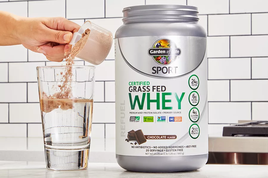 A hand pouring a scoop of Garden of Life SPORT Grass Fed Whey Protein Powder into a glass of water