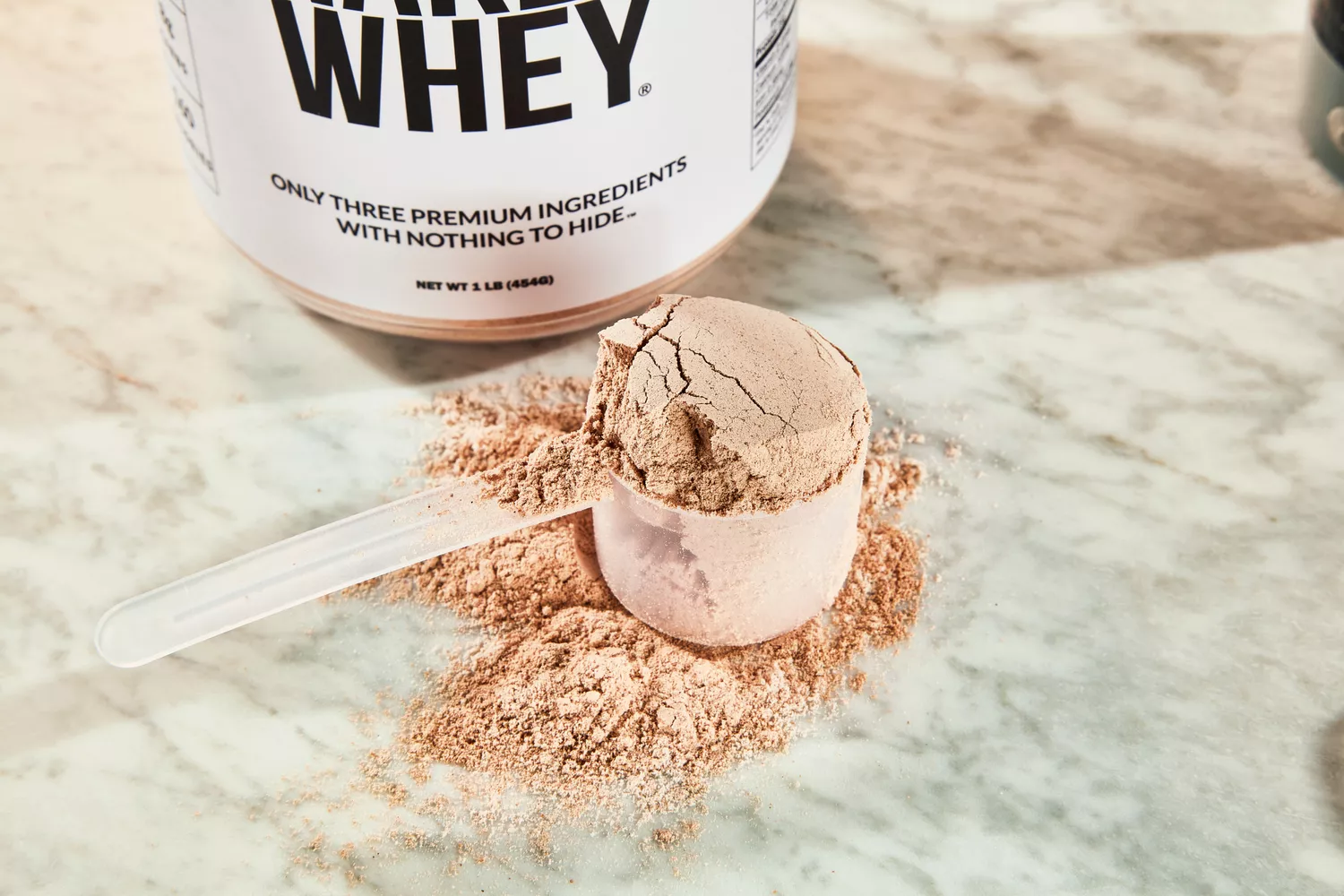 Scoop of Naked Whey Chocolate Protein Powder displayed on a marble counter