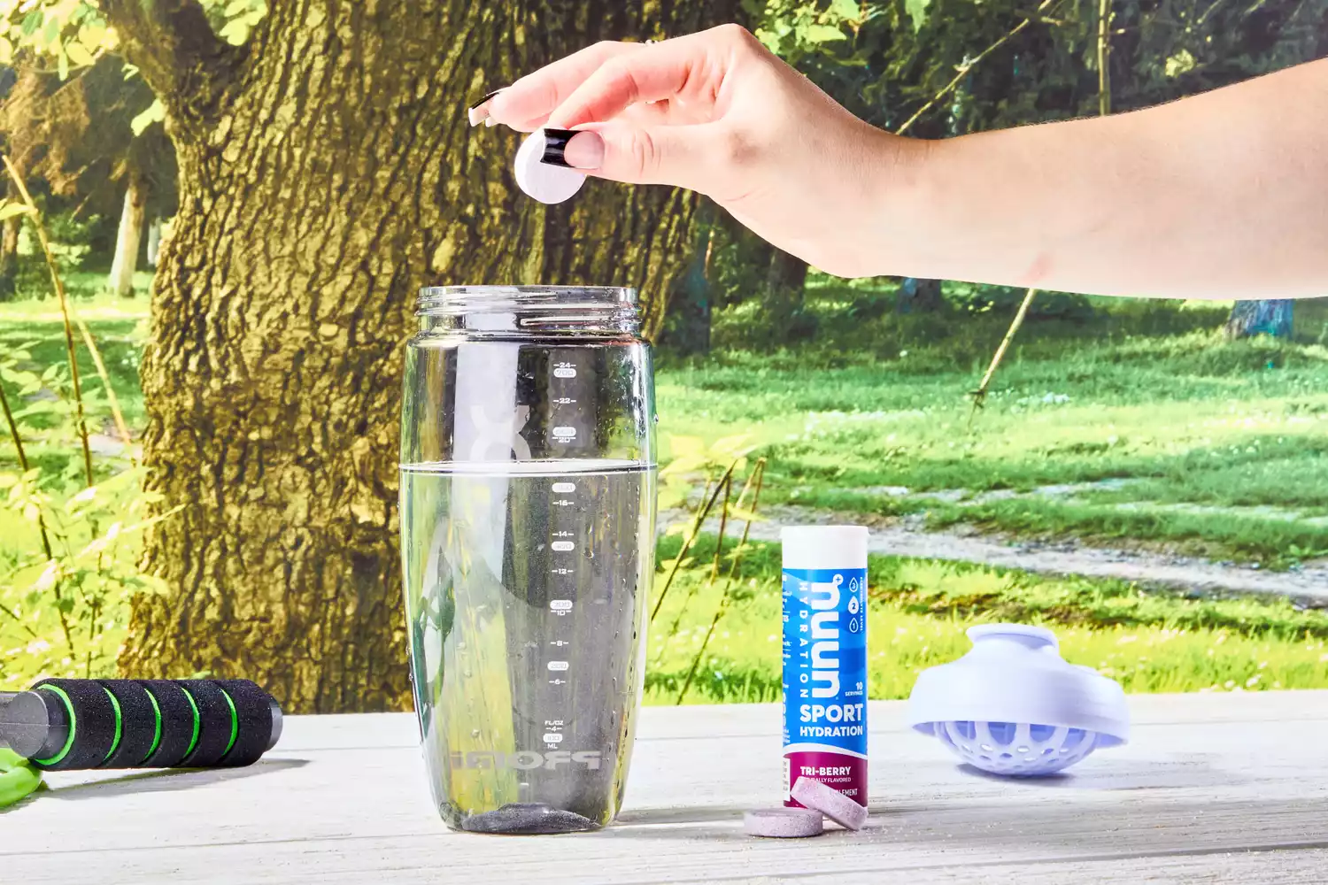 A hand adding a Nuun Sport Electrolyte Drink Tablet into a glass of water on a wooden table