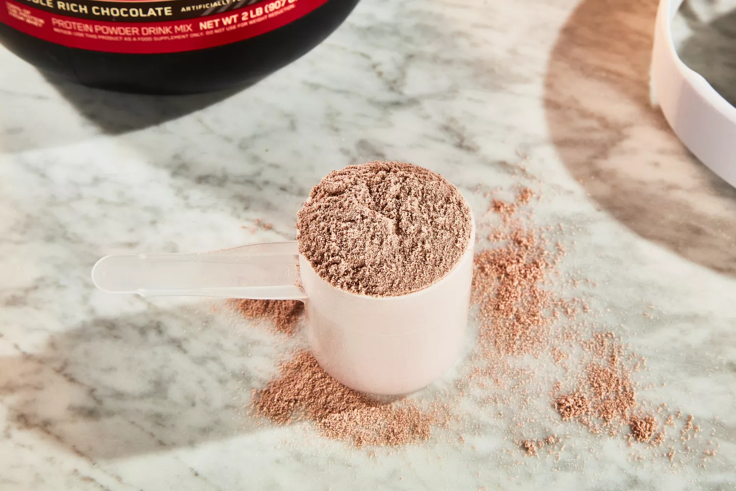 Optimum Nutrition Gold Standard 100% Whey Protein Powder in a scoop with powder on the table