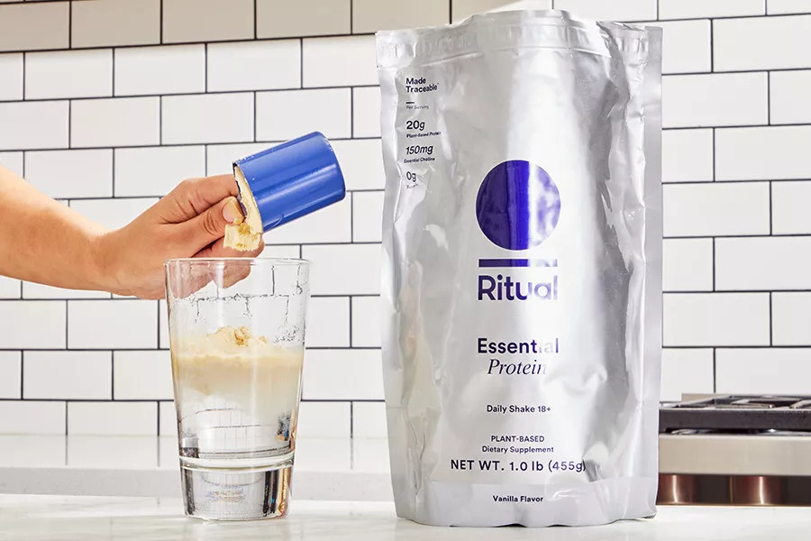 A person pours a scoop of Ritual Essential Protein Daily Shake into water