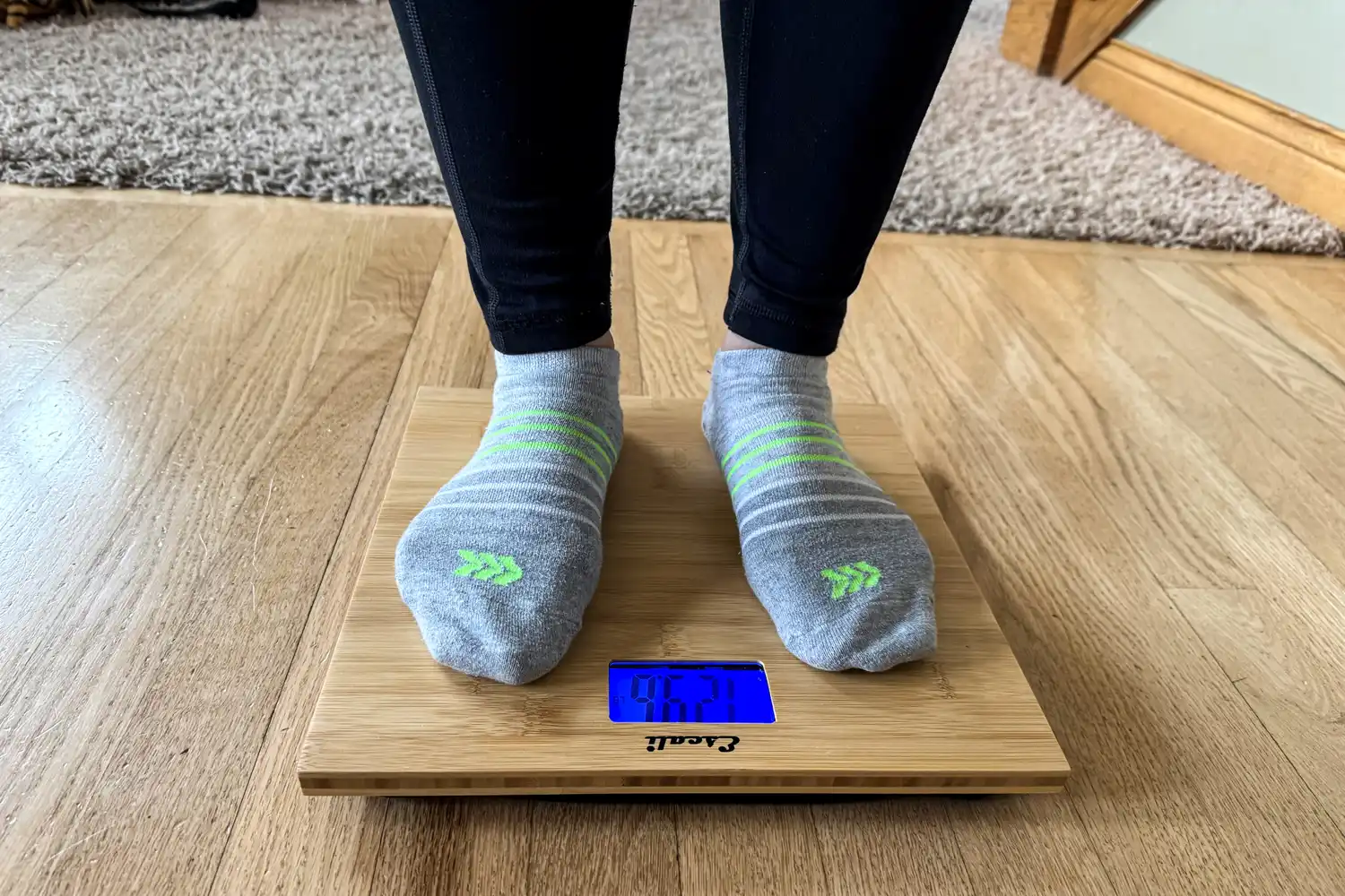 A front view of a person standing on the Escali Bamboo Digital Electronic Bathroom Scale in socks