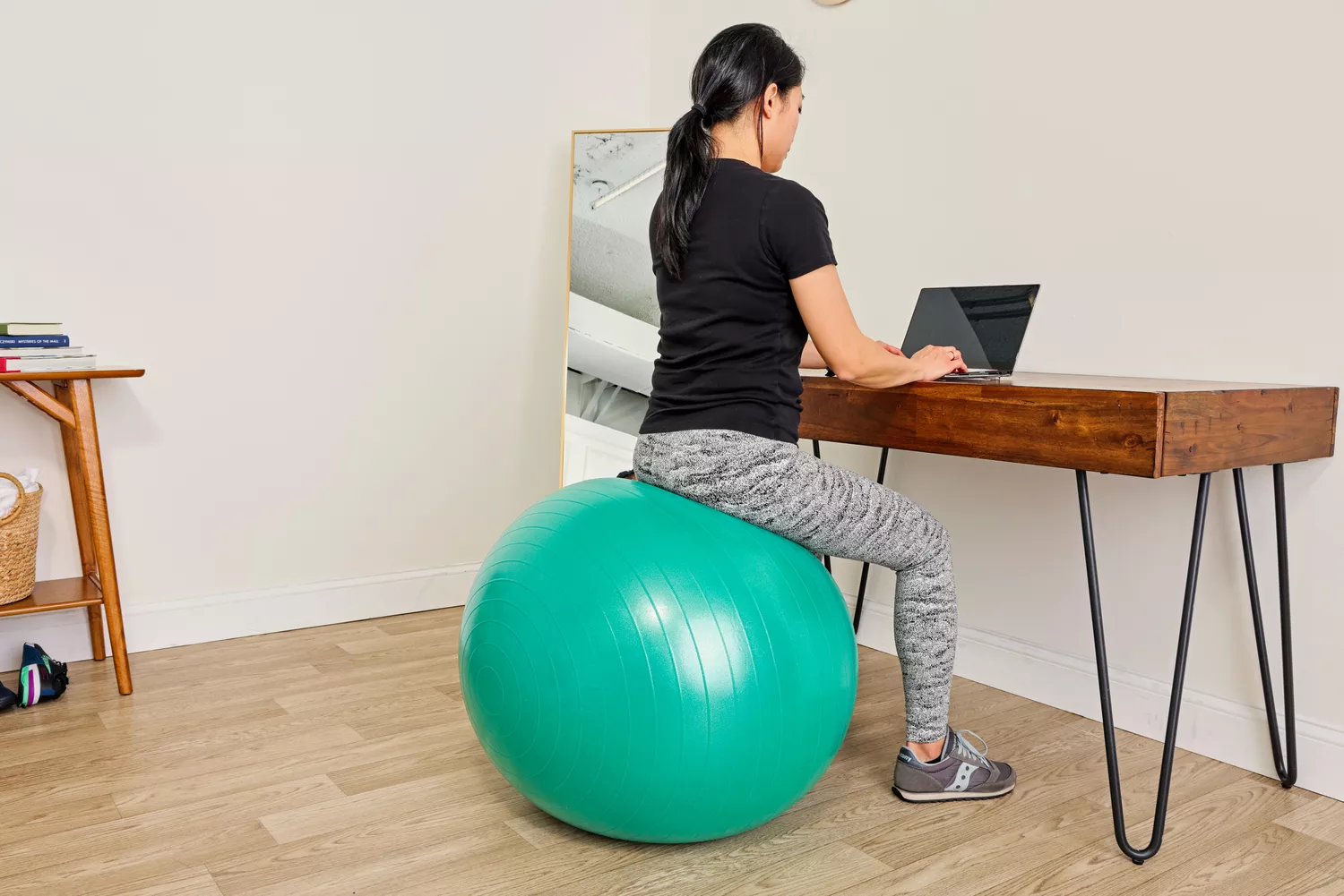 A person sits on the Gaiam Total Body Balance Ball Kit while working on a laptop