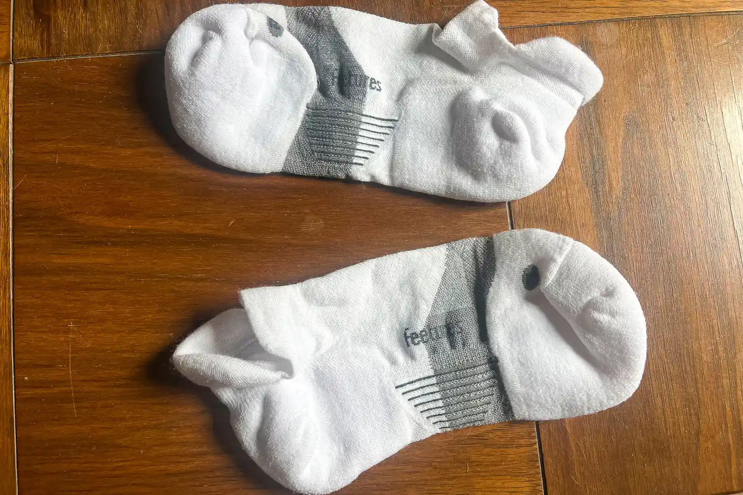 A pair of Feetures Merino 10 Max Cushion Tab Socks on a wooden floor