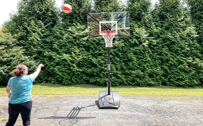 A person shoots a basketball into the Silverback NXT Portable Adjustable 10ft Outdoor Basketball Hoop