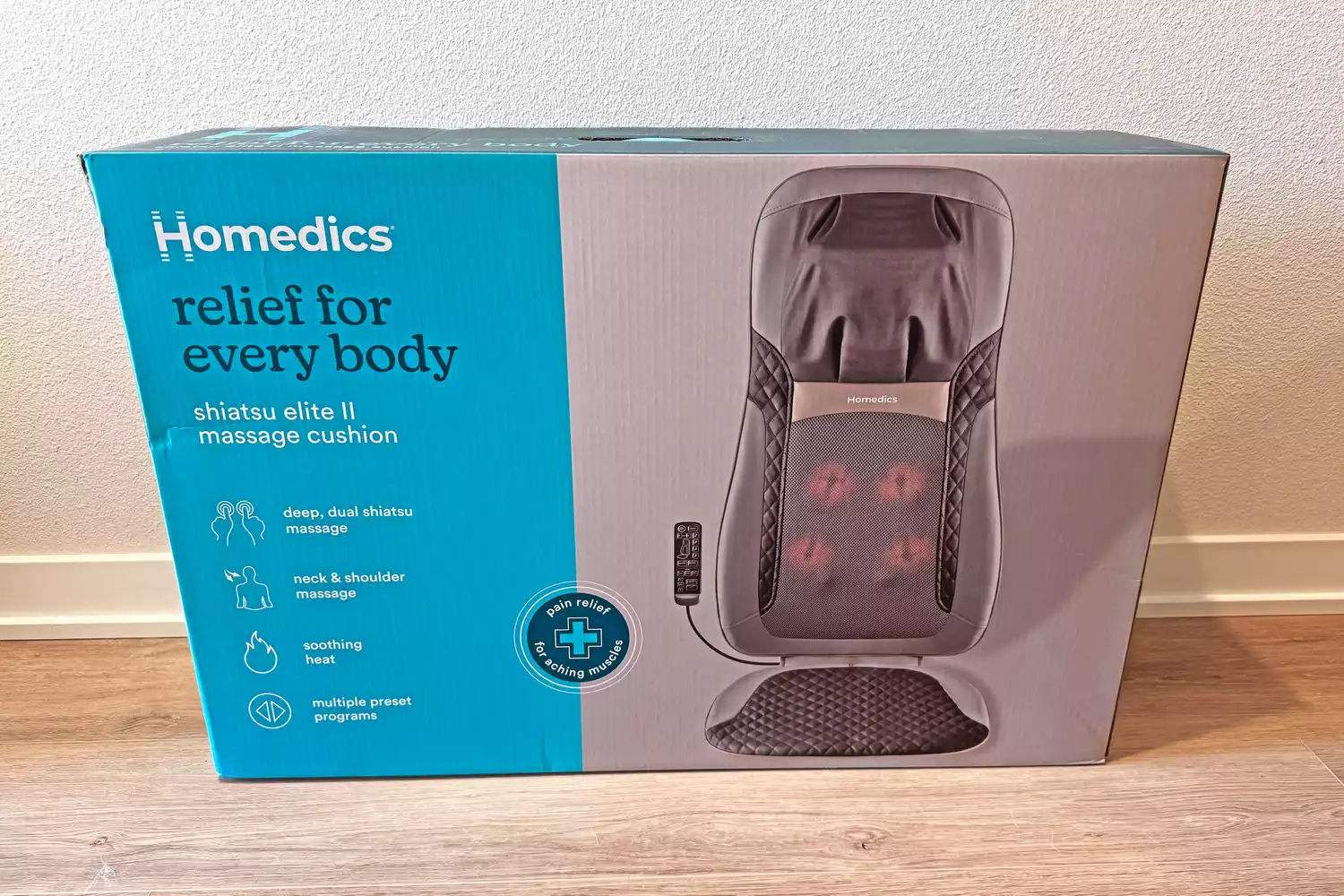 The Homedics Shiatsu Elite II Massage Cushion with Soothing Heat box on a wooden floor in front of a white wall