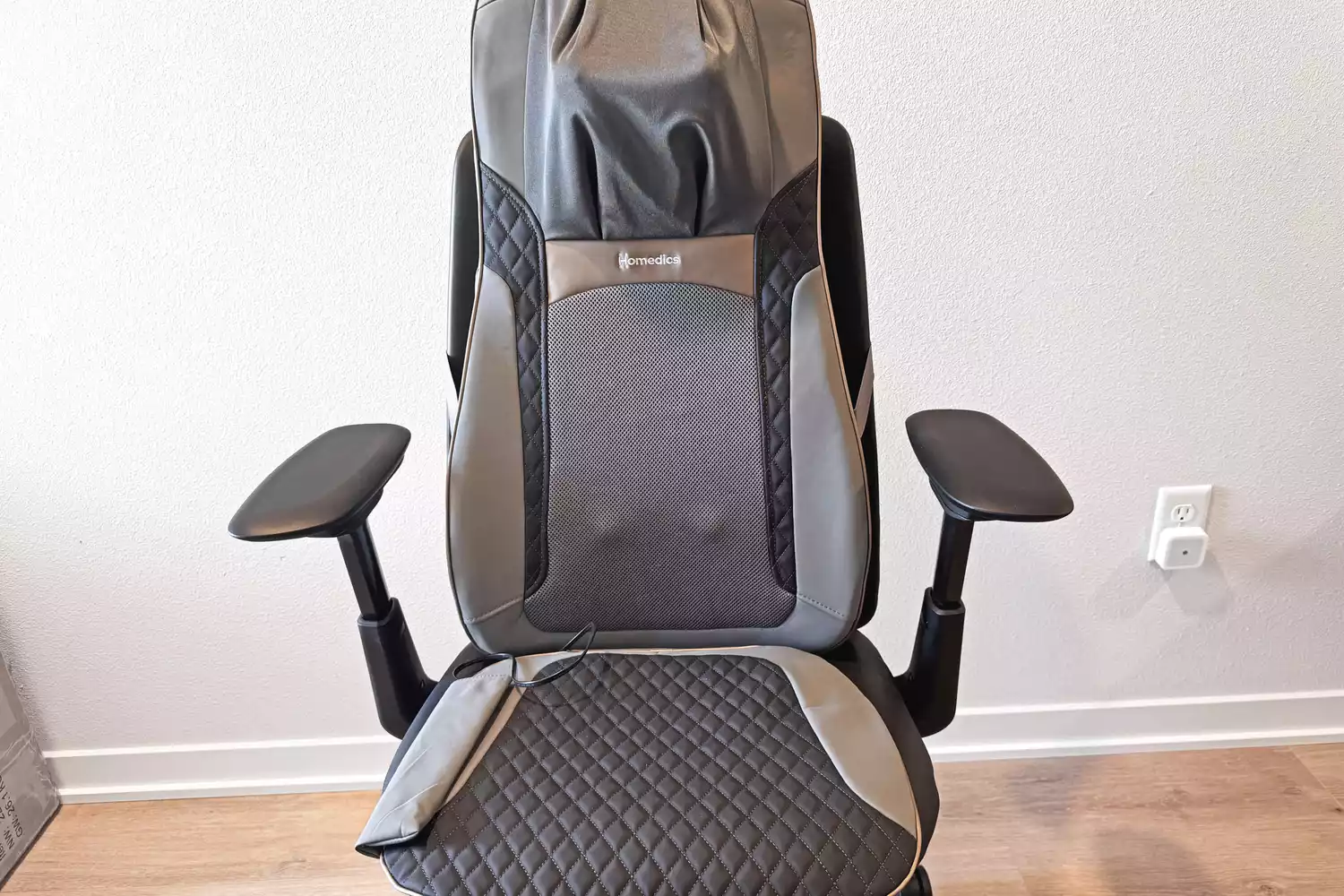 The Homedics Shiatsu Elite II Massage Cushion with Soothing Heat on a wooden floor in front of a white wall