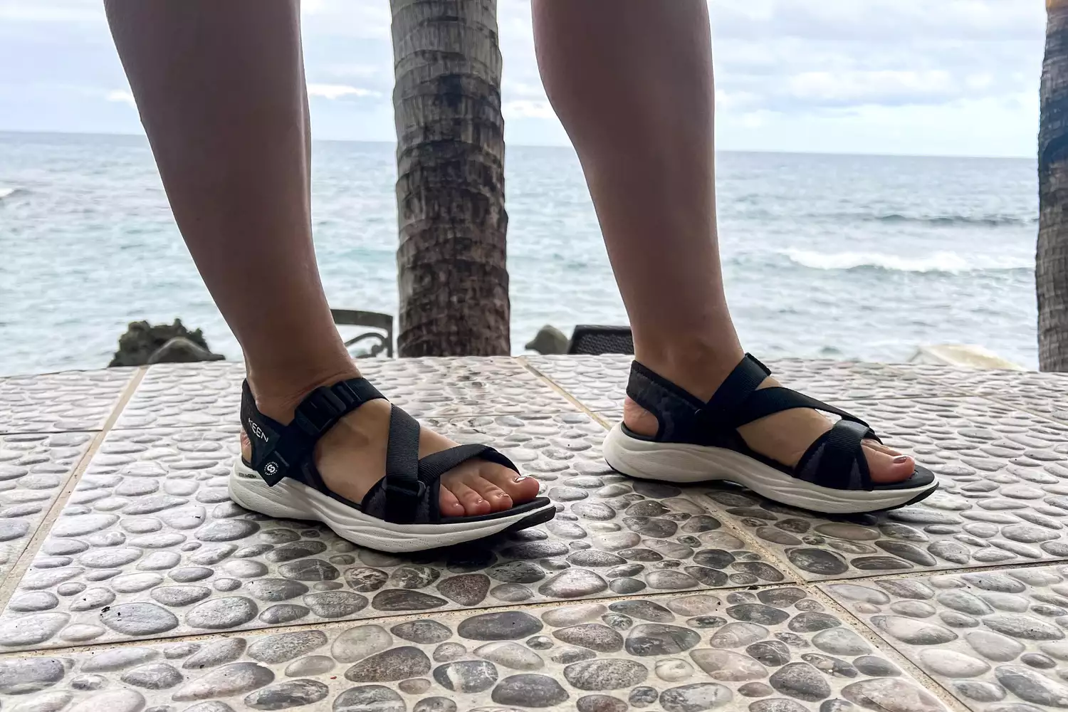 A close-up of legs wearing the Keen Women's Leiki Open-Toe Sandal on stones