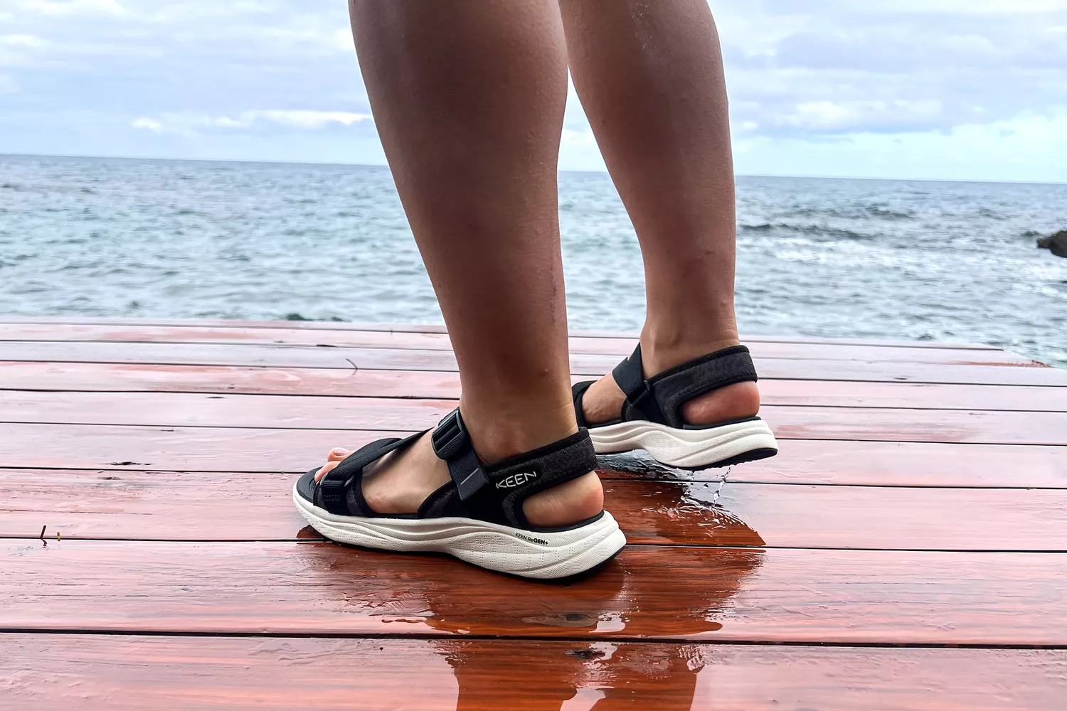 A close-up of the Keen Women's Leiki Open-Toe Sandal from the side worn on a dock