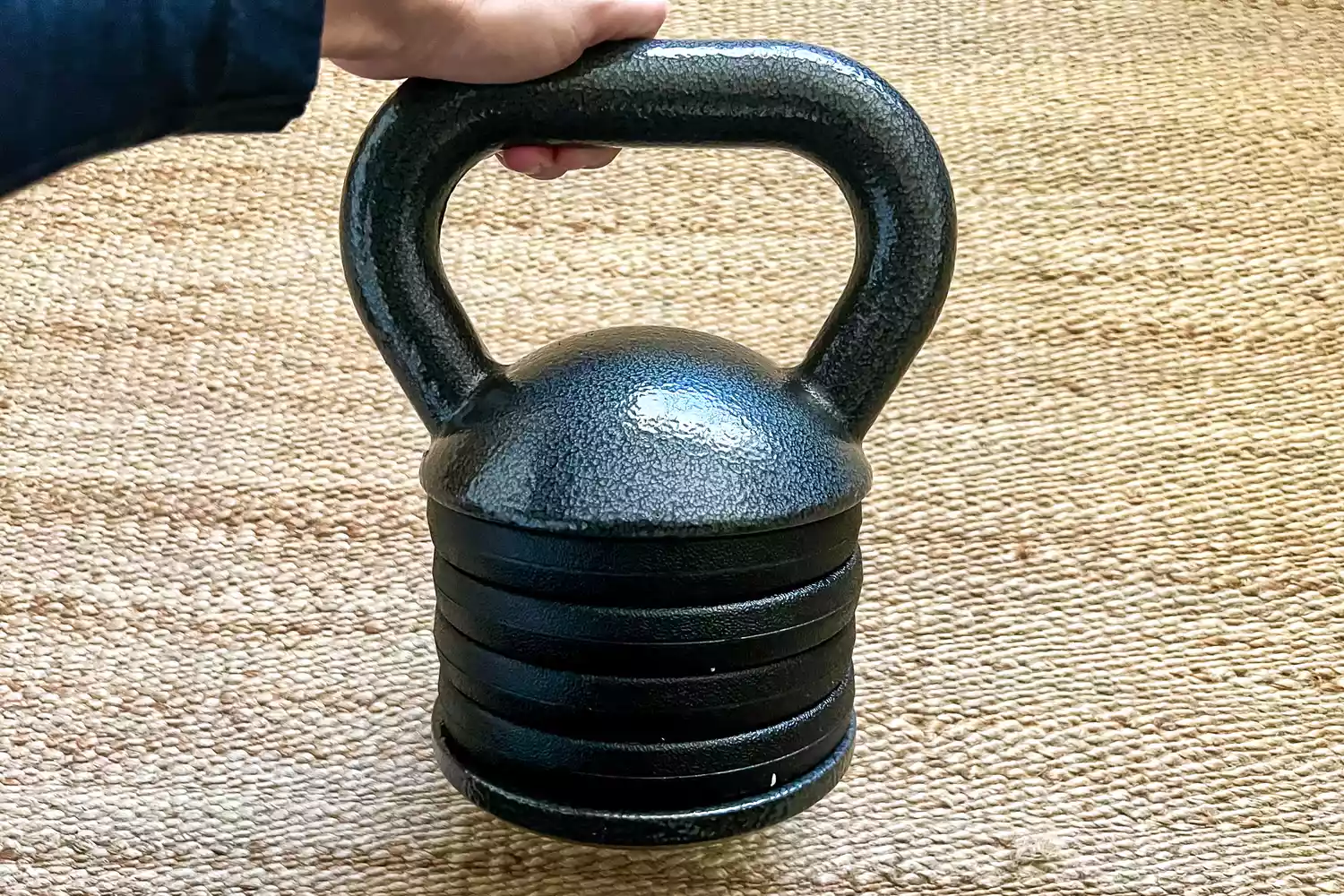 A person holds the handle of the Apex APKB-5009 Adjustable Heavy-Duty Kettlebell
