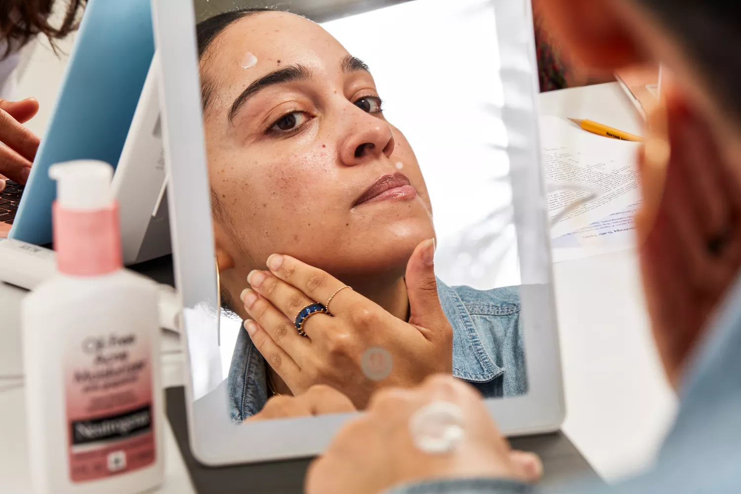 Person applying Neutrogena Pink Grapefruit Oil-Free Acne Moisturizer to their face while looking in a mirror