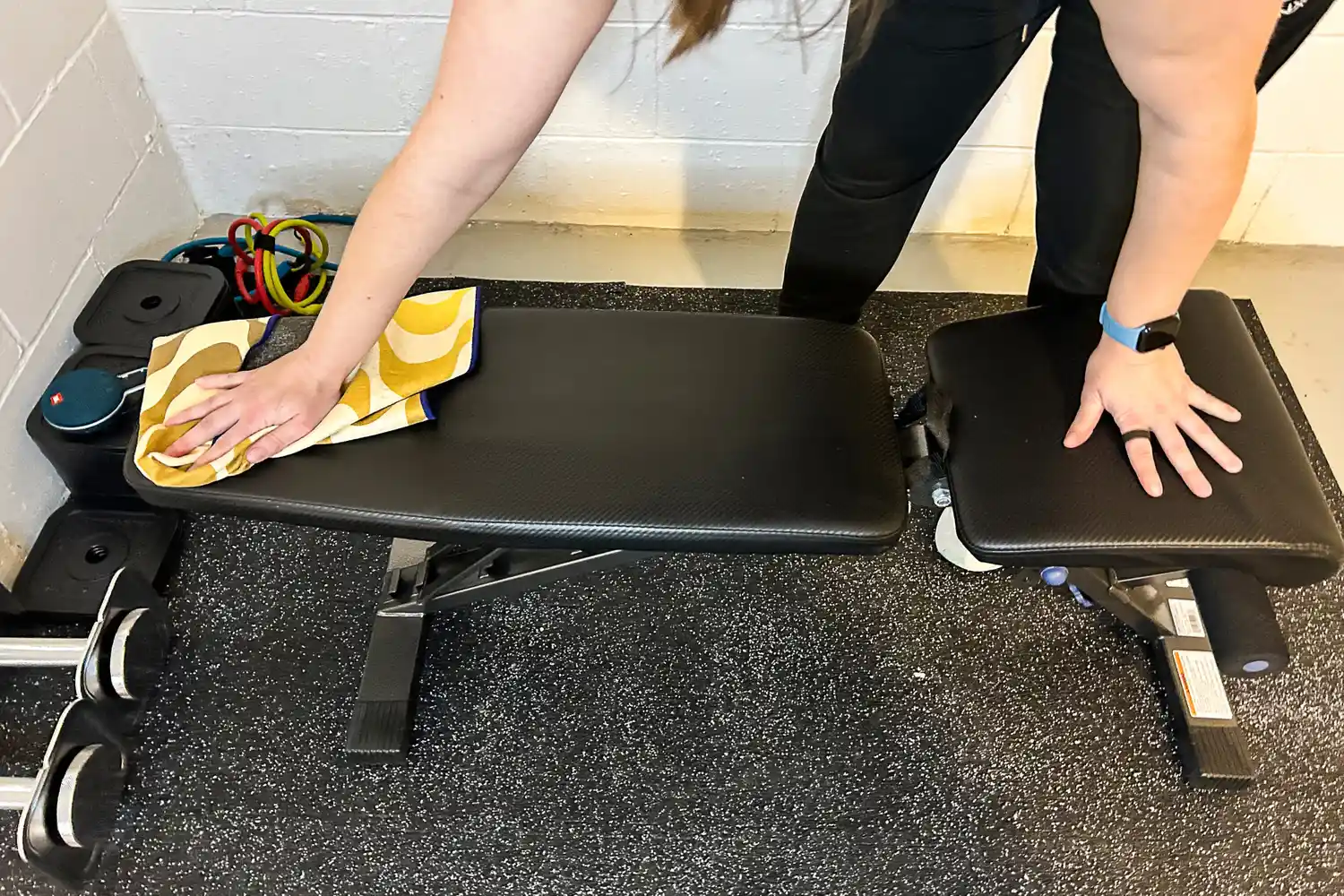 A person uses the Nomadix Fitness Towel to wipe down a workout bench