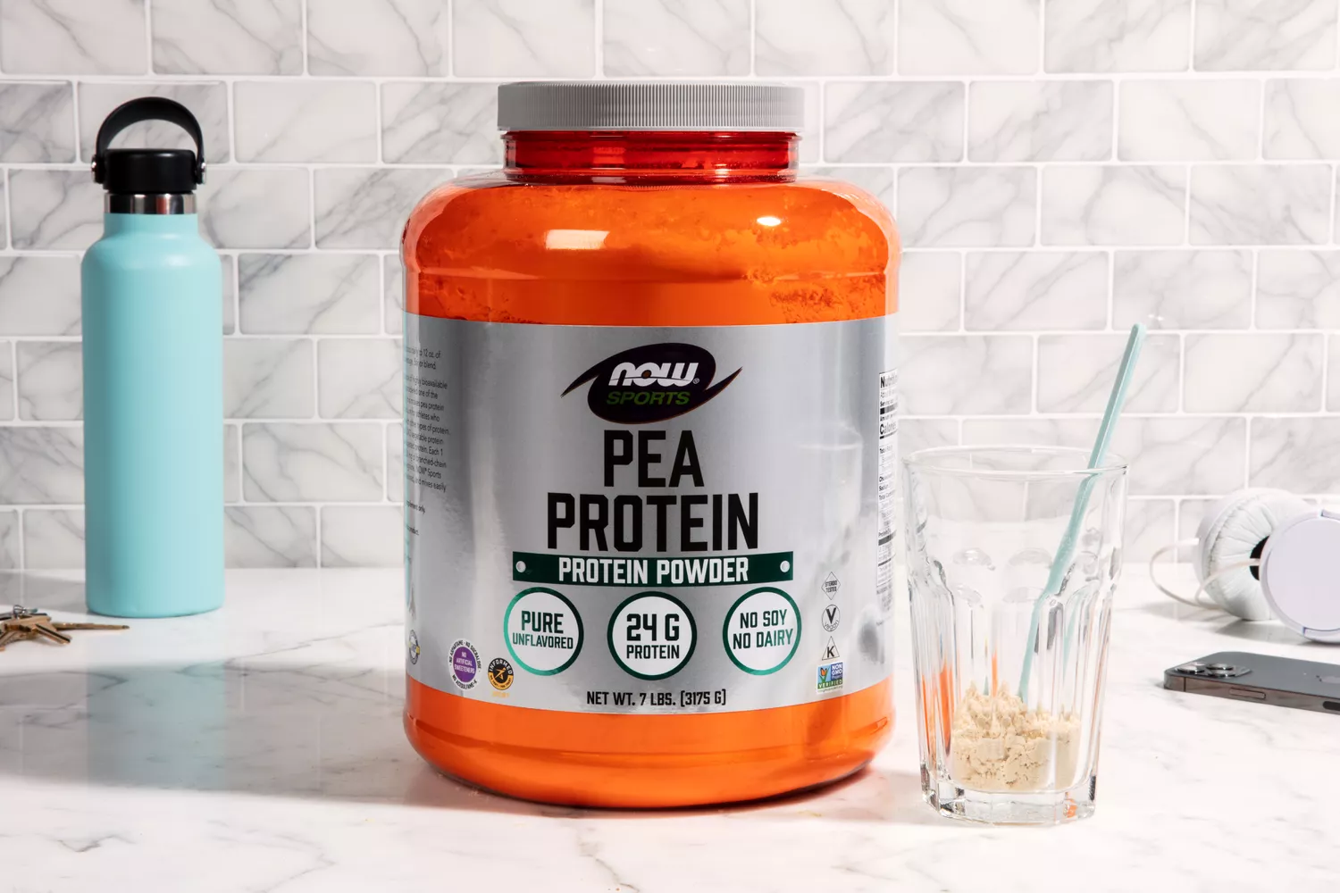 NOW Sports Pea Protein next to cup with filled with protein powder and water bottle on marble counter