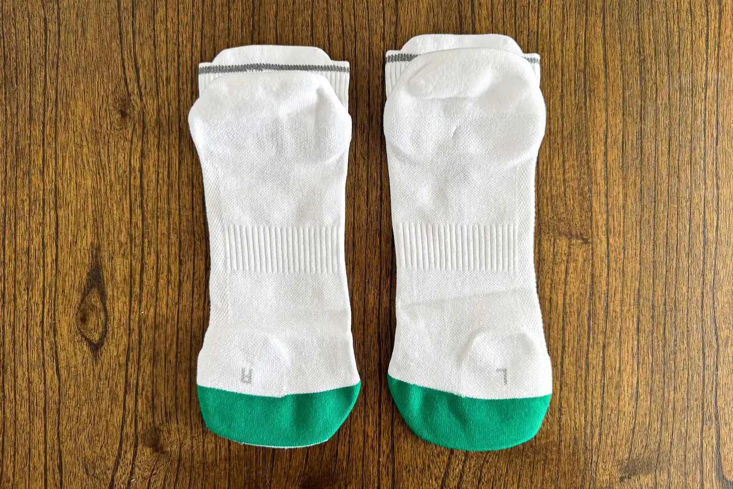 A pair of On Running Elite Run Sock Low on a wooden floor