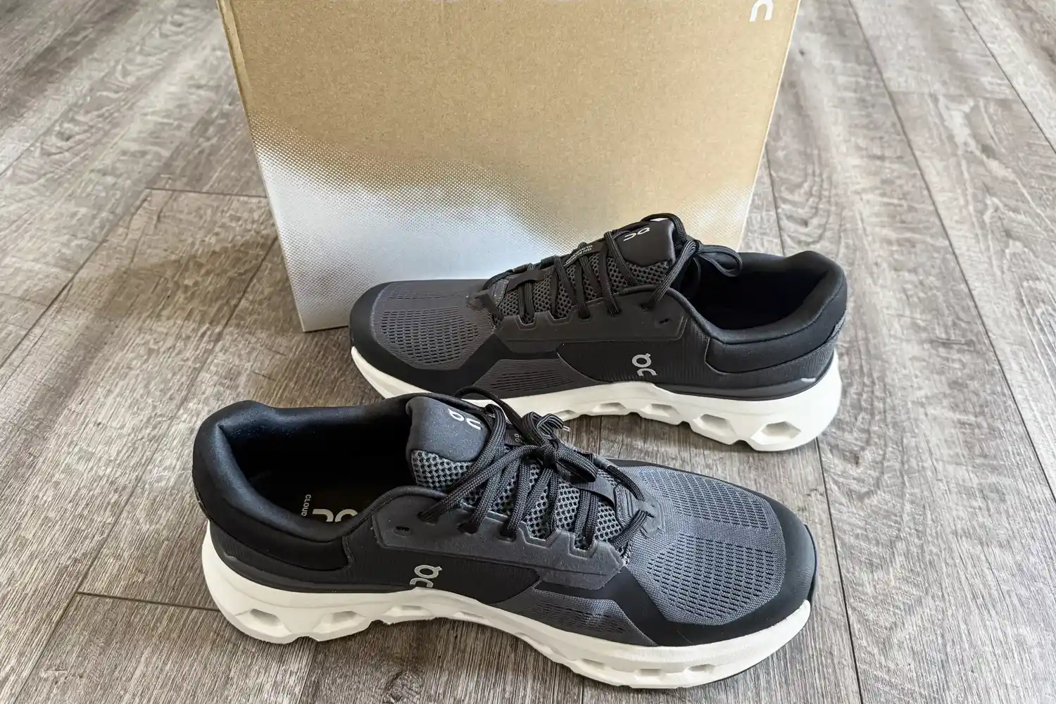A pair of On Running Men's Cloudrunner 2 Wide Running Shoes on a wooden floor