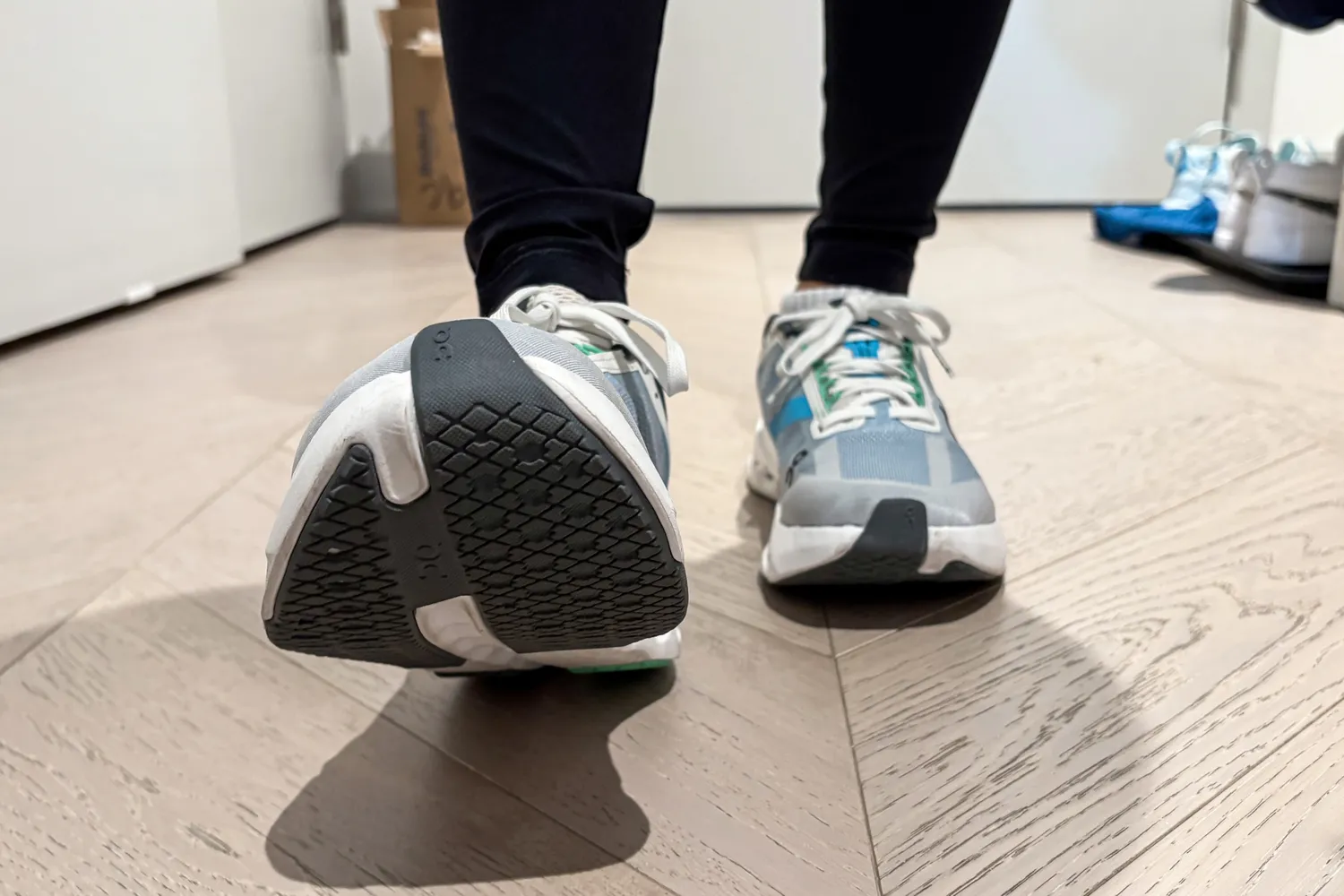 A person walks on a wooden floor while wearing the On Running Women's Cloudsurfer Next Wide Running Shoes