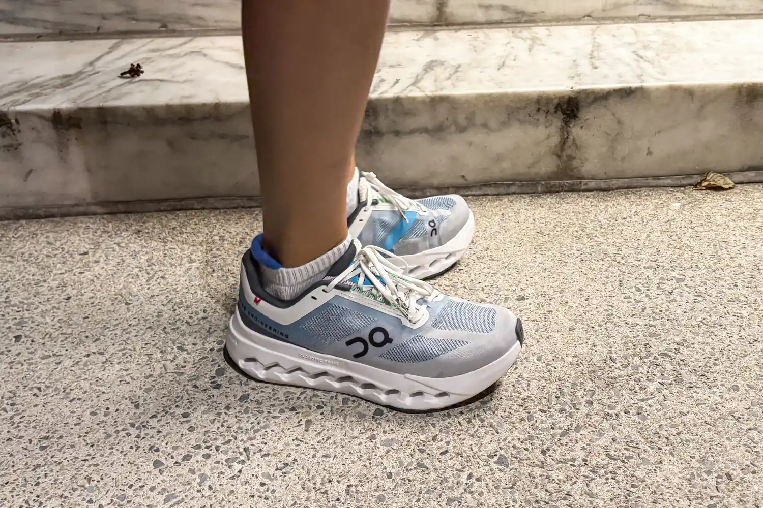 A side view of a person wearing the On Running Women's Cloudsurfer Next Wide Running Shoes