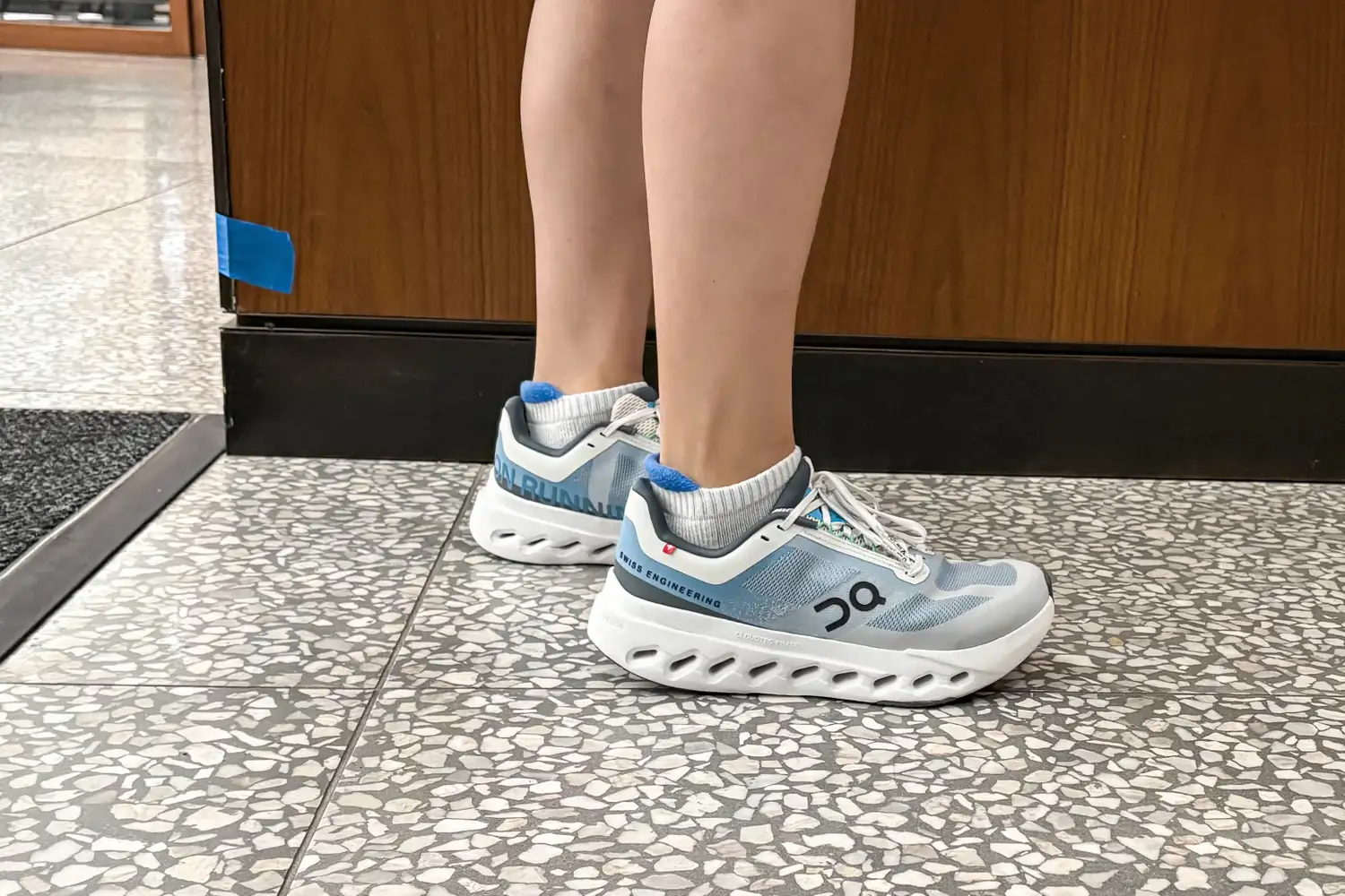 A side view of a person wearing the On Running Women's Cloudsurfer Next Wide Running Shoes