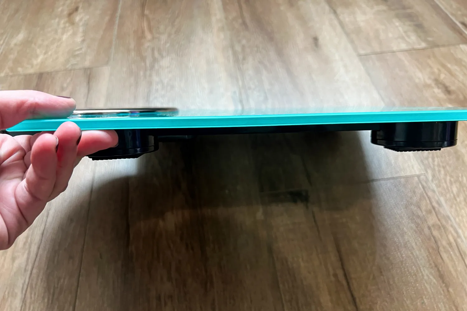 A person holds up the Ozeri Rev 400 lbs Bathroom Scale to show the thickness of the scale