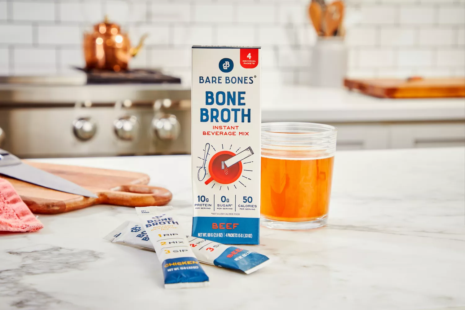 A box of Bare Bones Bone Broth Instant Powdered Beverage Mix with packets and prepared broth on countertop