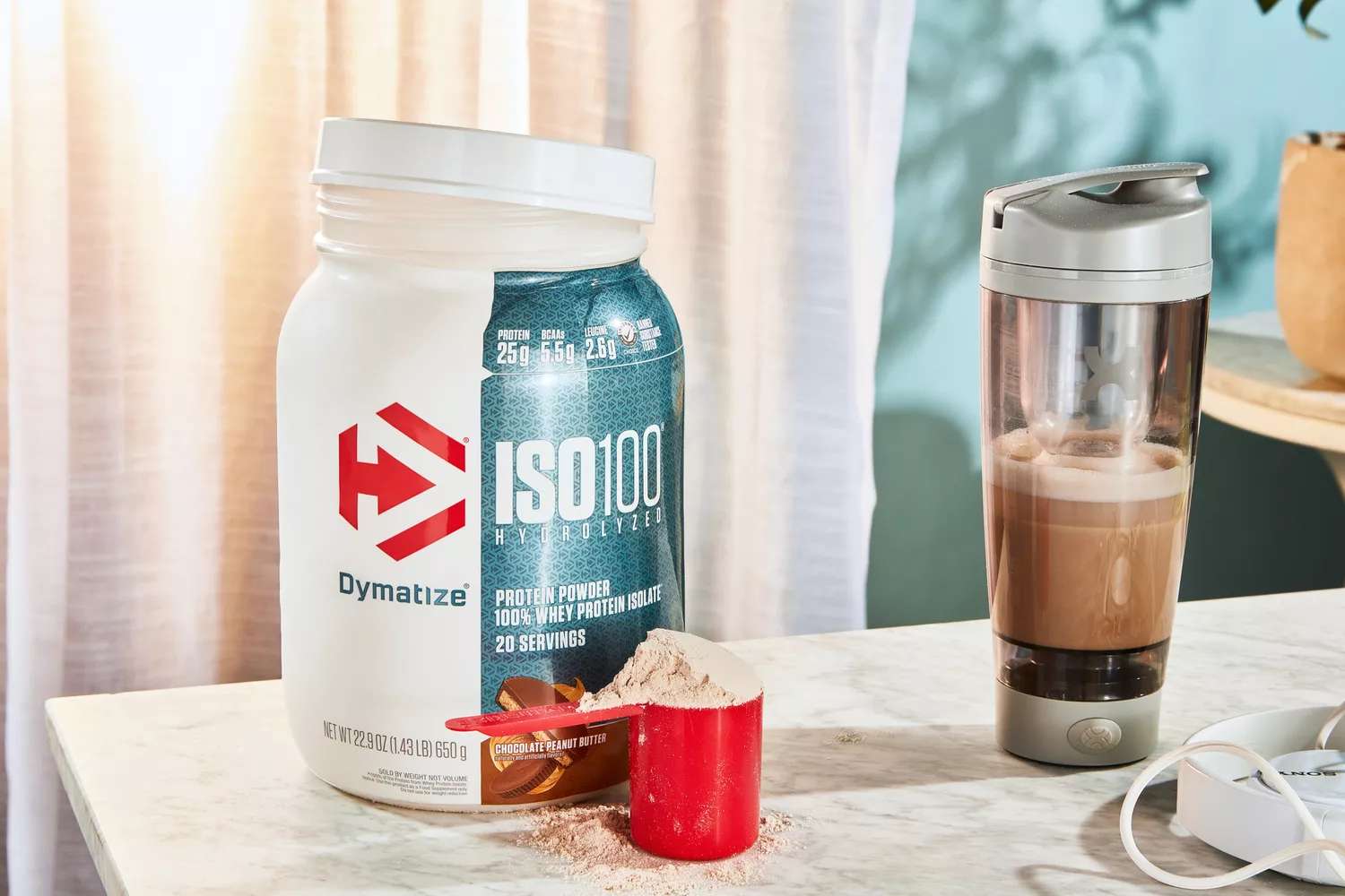 Dymatize ISO100 Whey Protein Powder Chocolate Peanut Butter in a scoop next to its container and a blender bottle