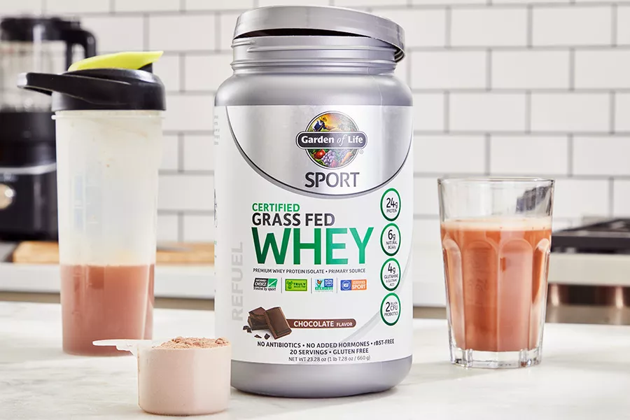 Garden of Life SPORT Grass Fed Whey Protein Powder with a scoop, blender bottle, and protein shake in a glass on counter