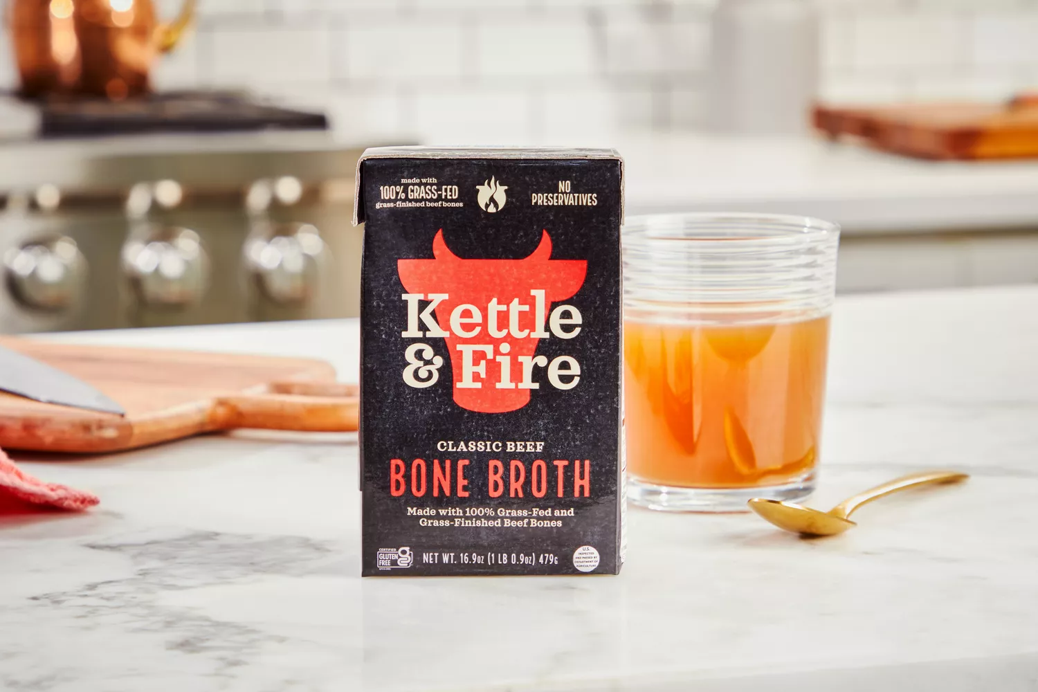 A box of Kettle &amp; Fire Bone Broth and glass of broth on kitchen countertop