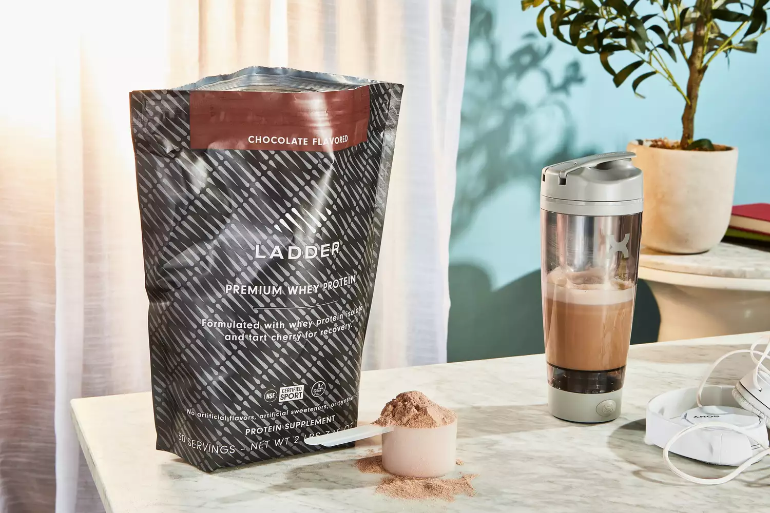 Ladder Whey Protein Powder in a scoop next to its container and a blender bottle