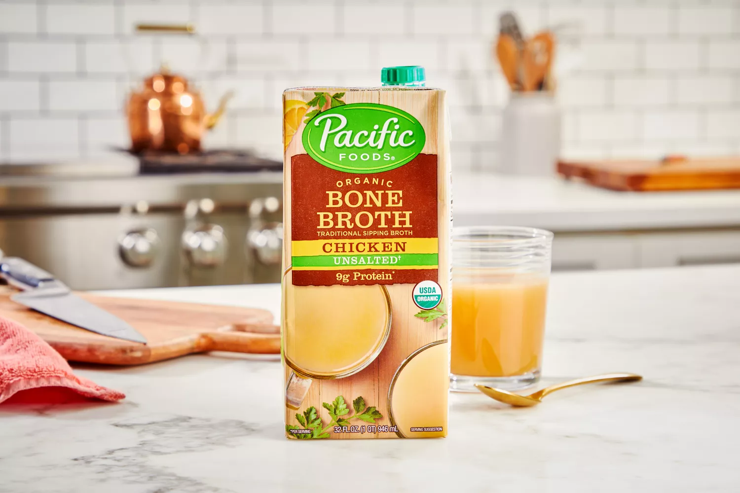 A box of Pacific Foods Chicken Bone Broth in front of glass of broth on countertop