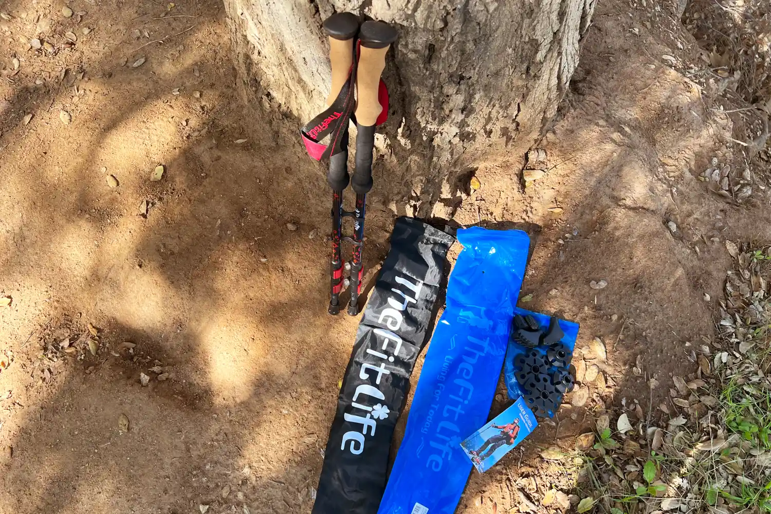 A pair of trekking poles protective caps and accessories placed beside a tree on the ground