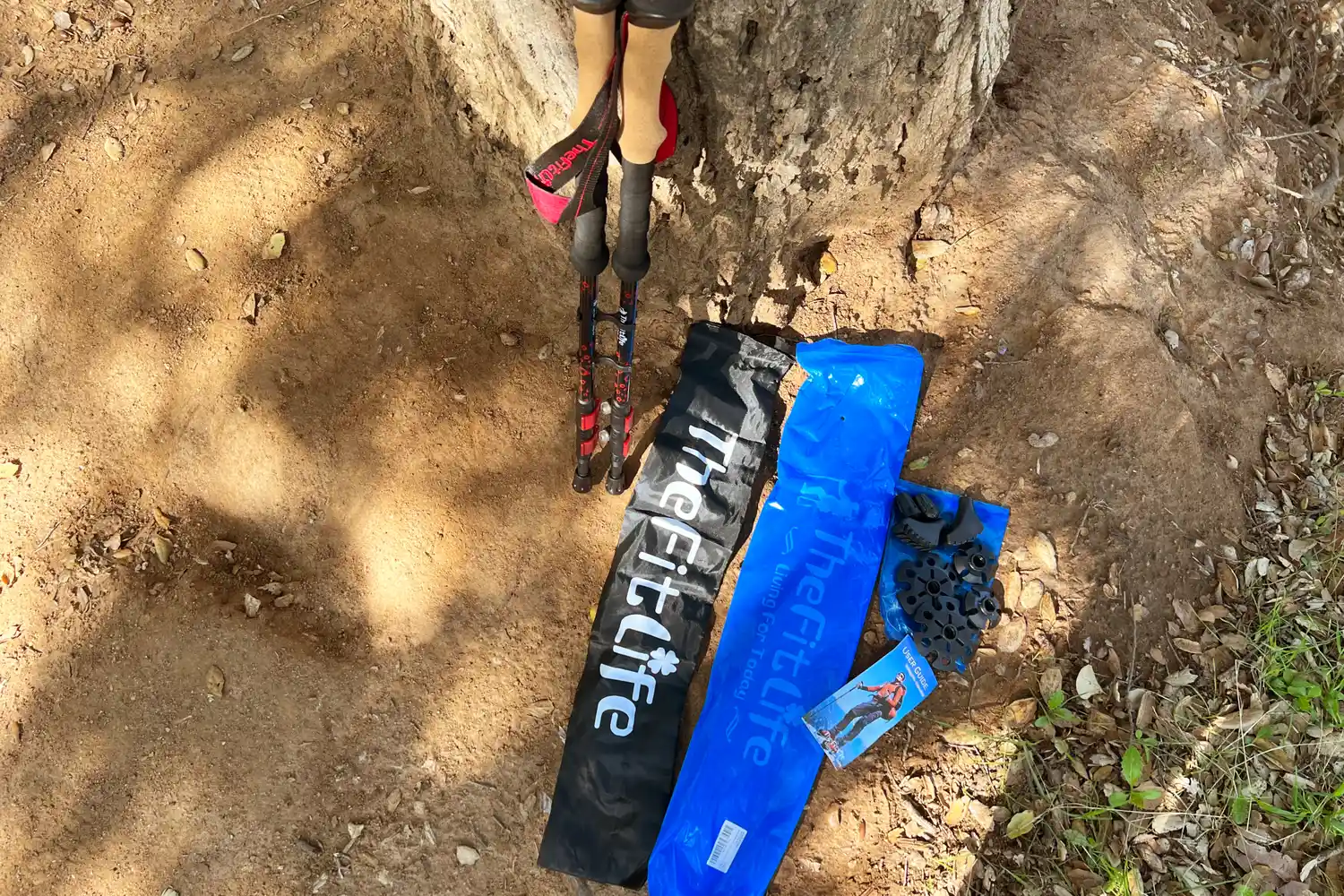 Hiking accessories and poles placed near the base of a tree on dirt ground