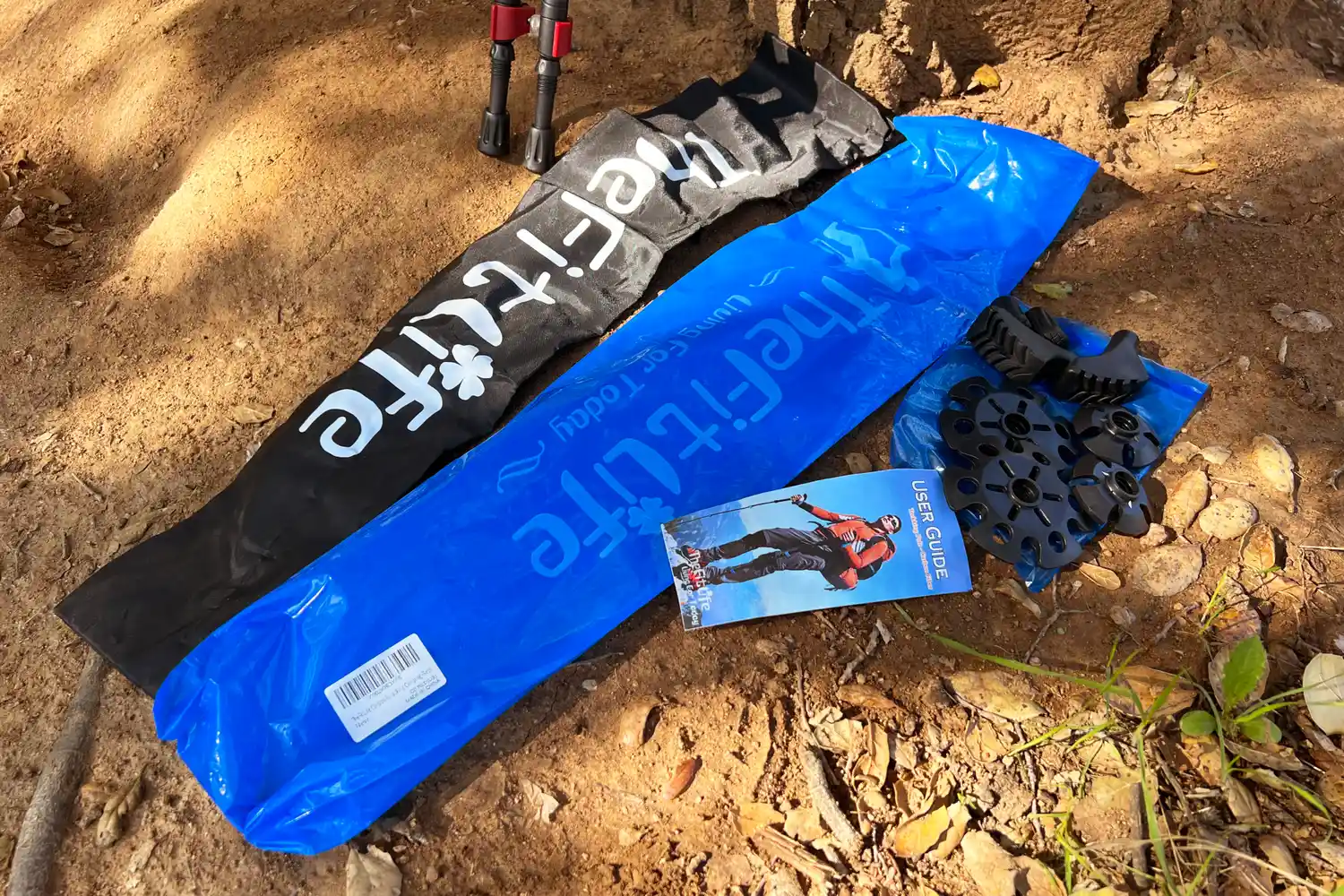 Hiking equipment including trekking poles bags spare tips and a user guide placed on the ground