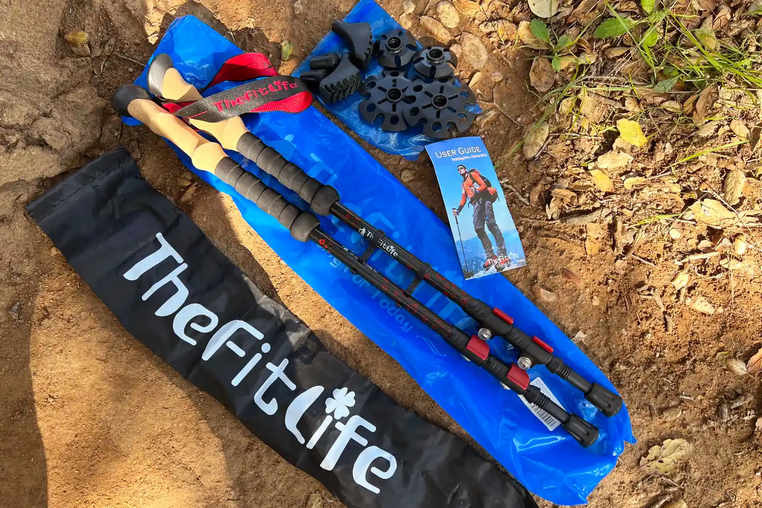 A set of trekking poles and accessories on the ground including a carrying bag extra tips and a user guide