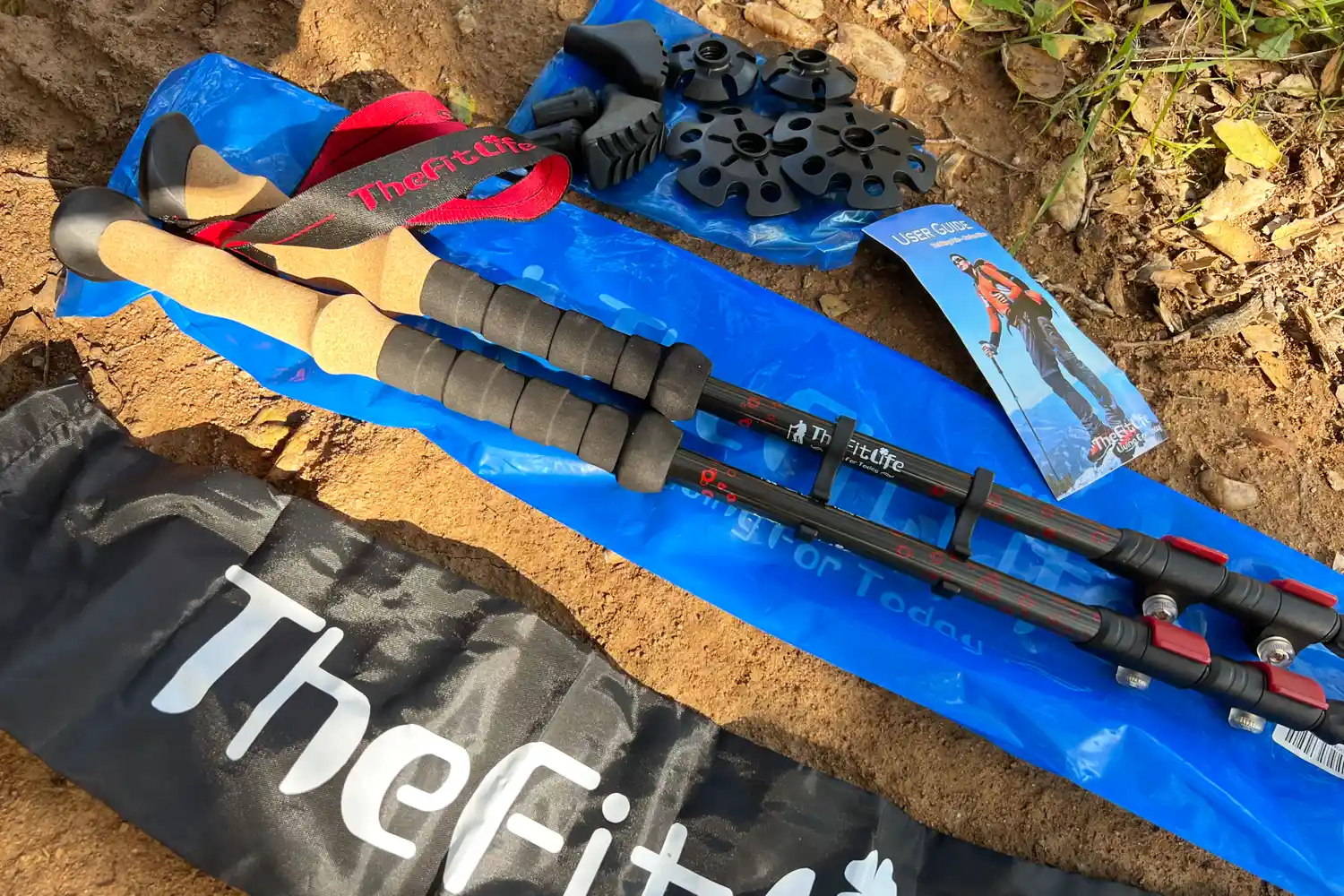 A set of trekking poles and accessories laid out on the ground including TheFitLifebranded components and a user manual