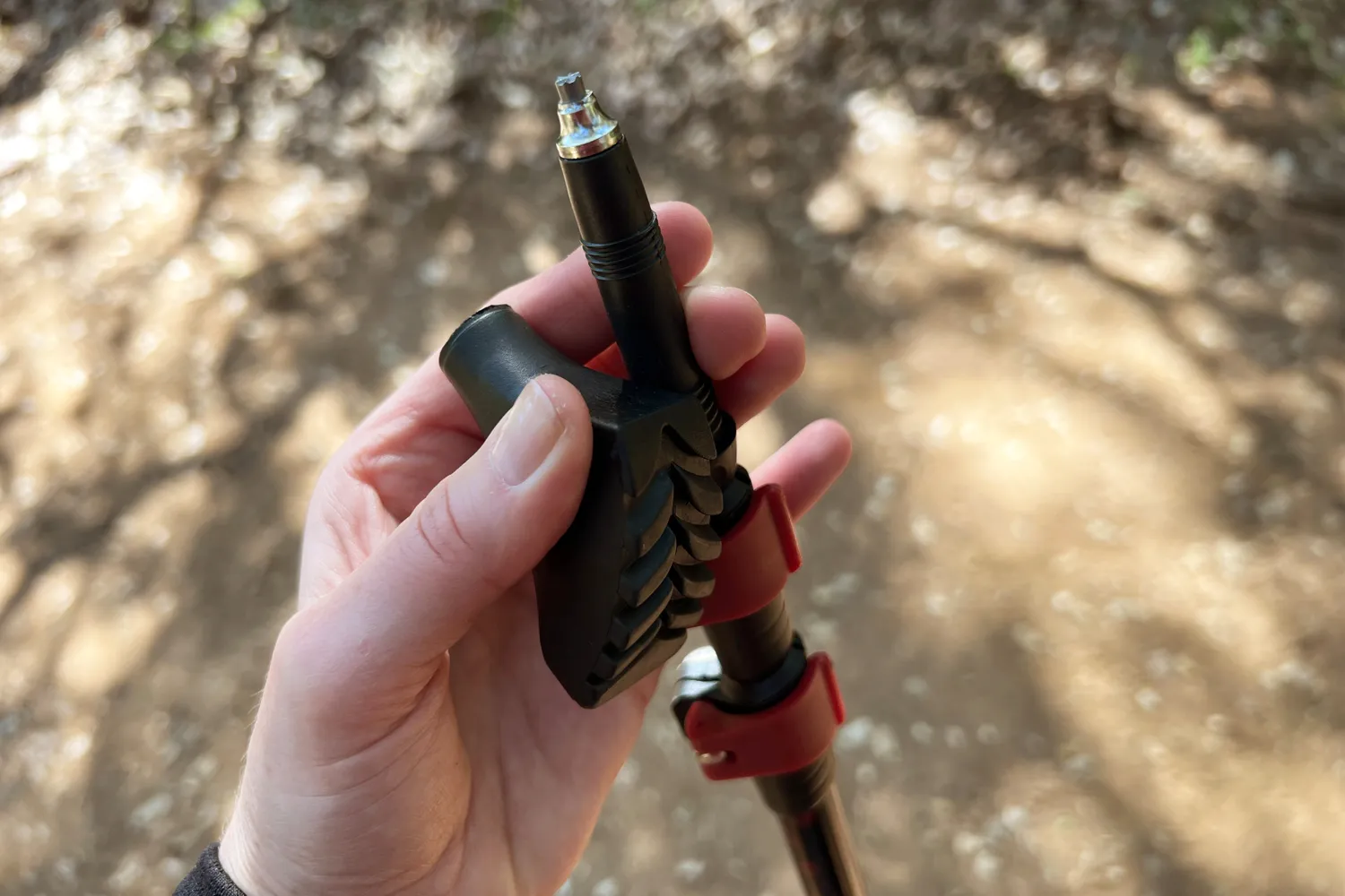 Hand holding a trekking pole tip and its attachment mechanism on a trail