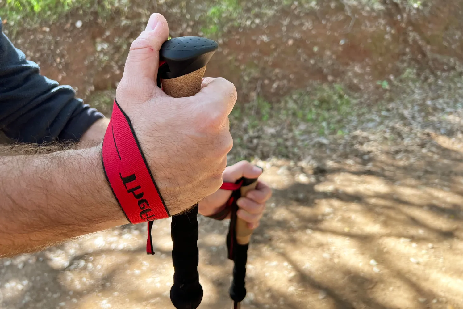 Hands holding trekking poles outdoors red straps visible on wrists